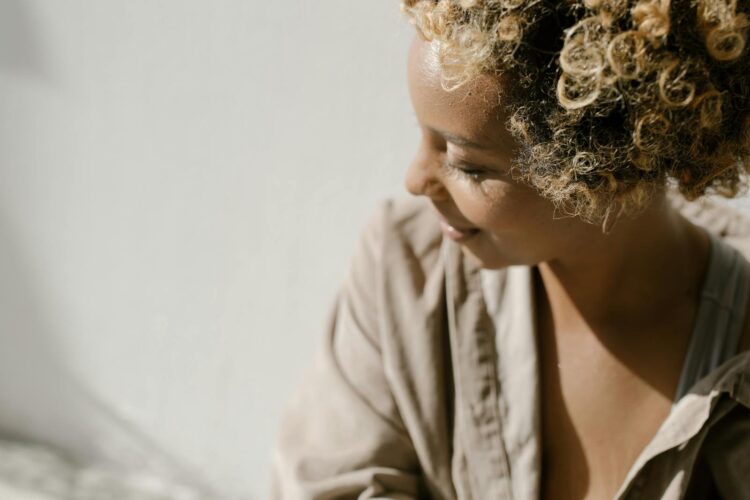 A woman with curly hair is smiling softly indoors in natural light.