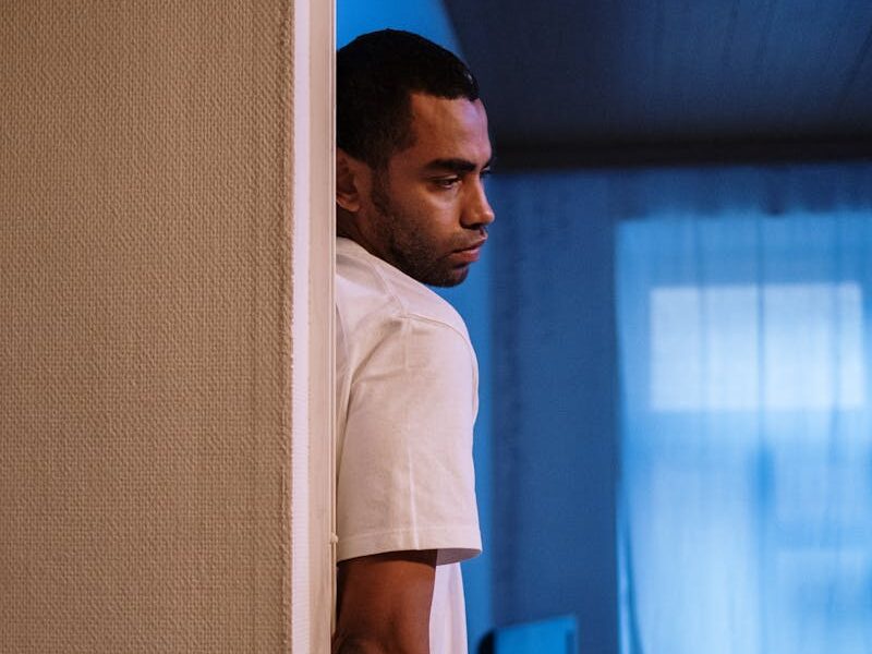 A man stands pensively in a dimly lit room, capturing a moment of deep thought.