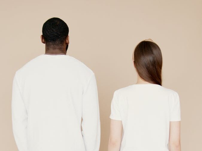 A diverse couple stands back to camera in casual white shirts, perfect for fashion concepts.