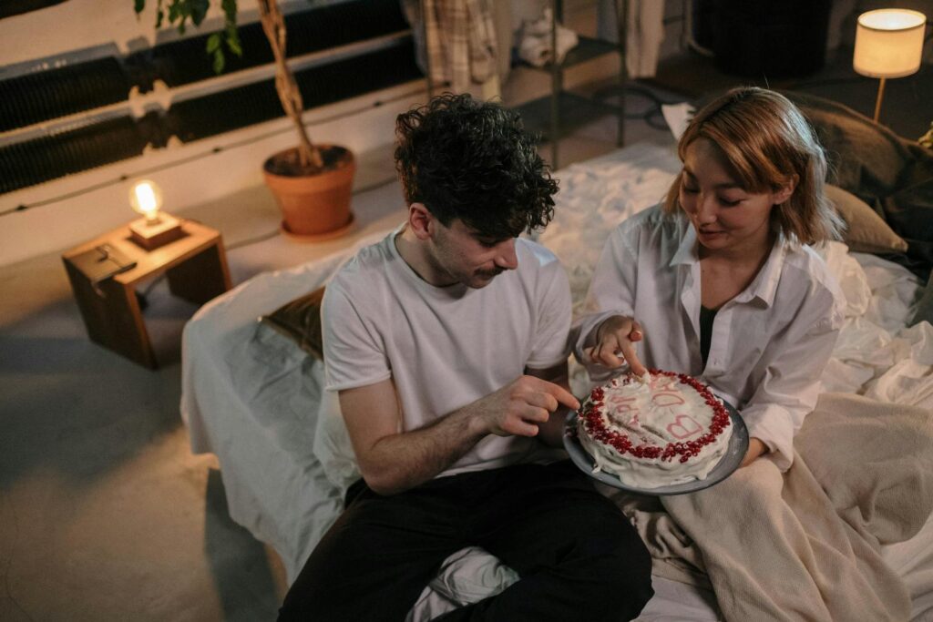 A couple enjoying a quiet birthday celebration with cake in a cozy bedroom setting.