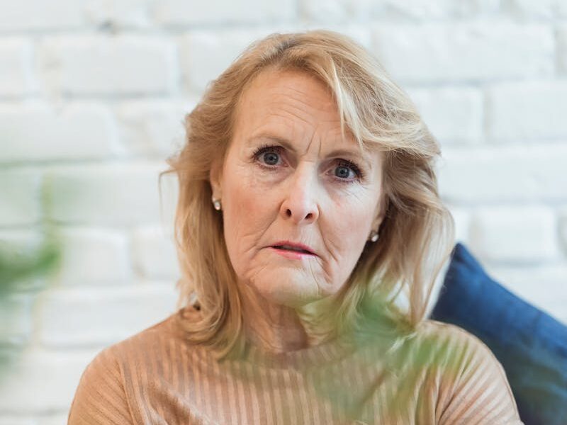 Serious elderly female in clothes with striped ornament looking at camera while sitting on sofa at home