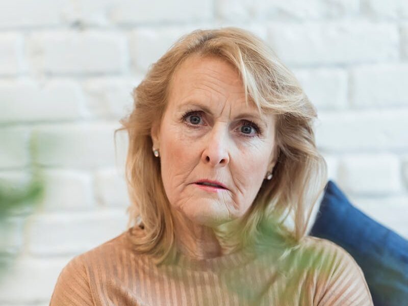 Serious elderly female in clothes with striped ornament looking at camera while sitting on sofa at home