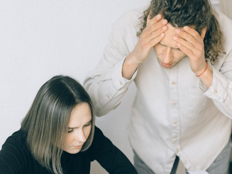 Young couple in discussion over financial papers, looking stressed at a table indoors.