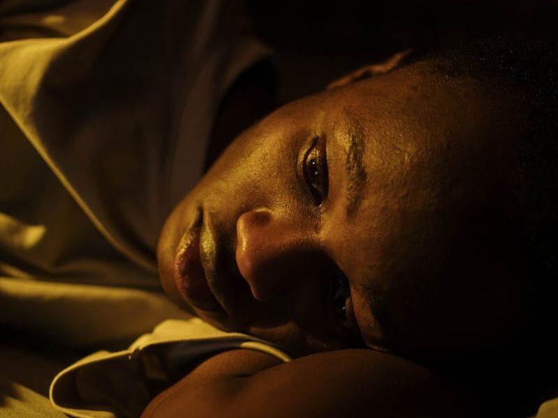A young man lying awake in bed, reflecting insomnia and mental exhaustion.