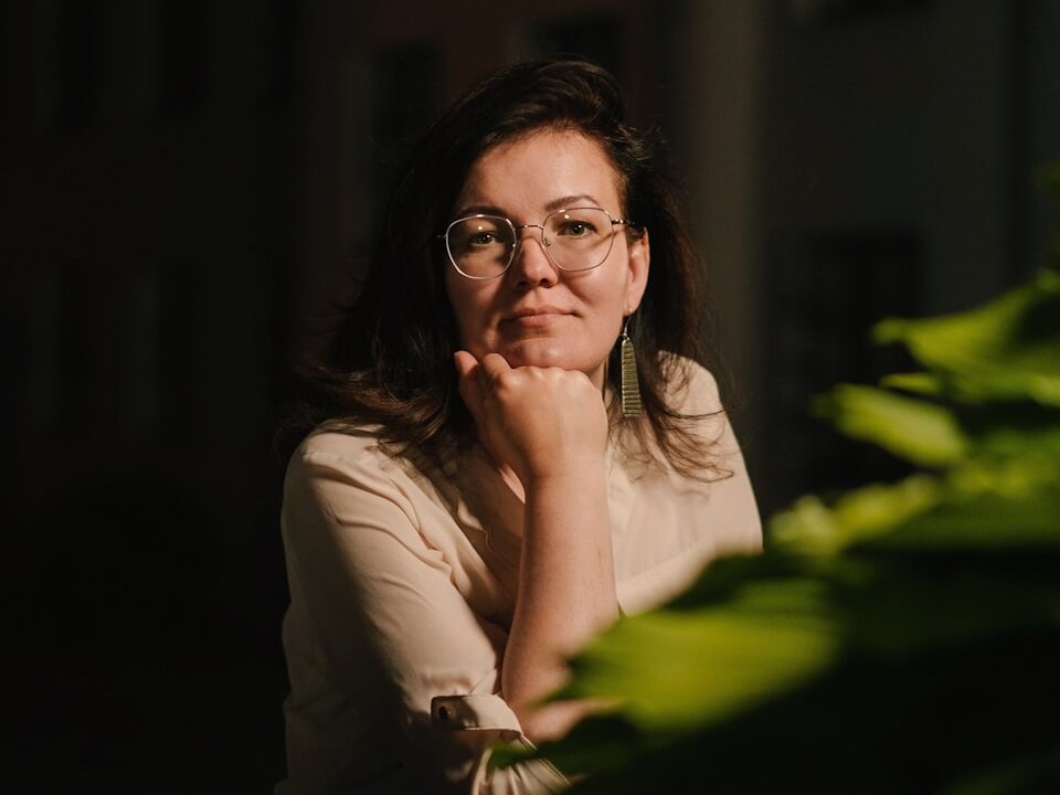 a woman wearing glasses sitting in front of a plant