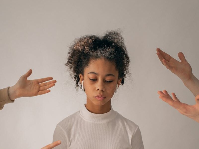 Crop people scolding disappointed African American teenage girl in casual wear standing on white background with sad face in studio