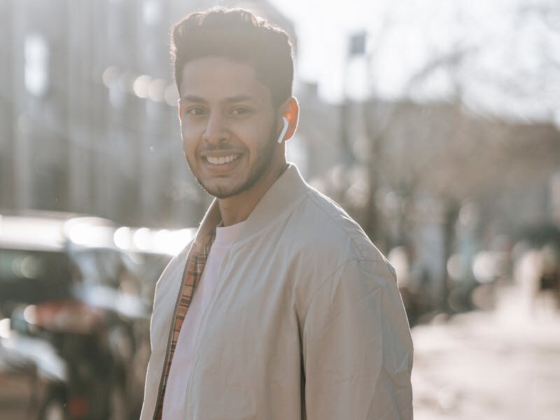 Young man with earphones smiling on a sunny street, enjoying music and leisure time outdoors.