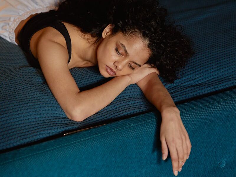 Thoughtful woman with curly hair lying on bed, expressing contemplation and calmness.