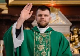 A priest in green vestments giving a blessing at the church altar.
