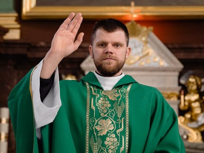A priest in green vestments giving a blessing at the church altar.