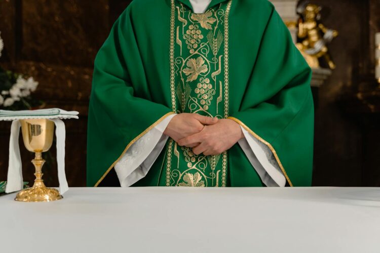 A priest in green embroidered robes standing behind an altar with a chalice during a Catholic mass.