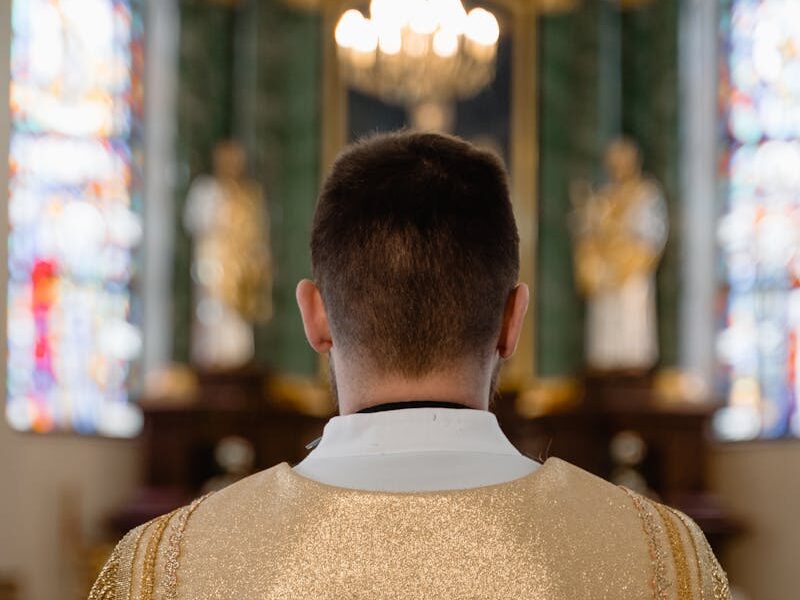 Back view of a priest in golden vestment, standing inside a cathedral during a religious ceremony.