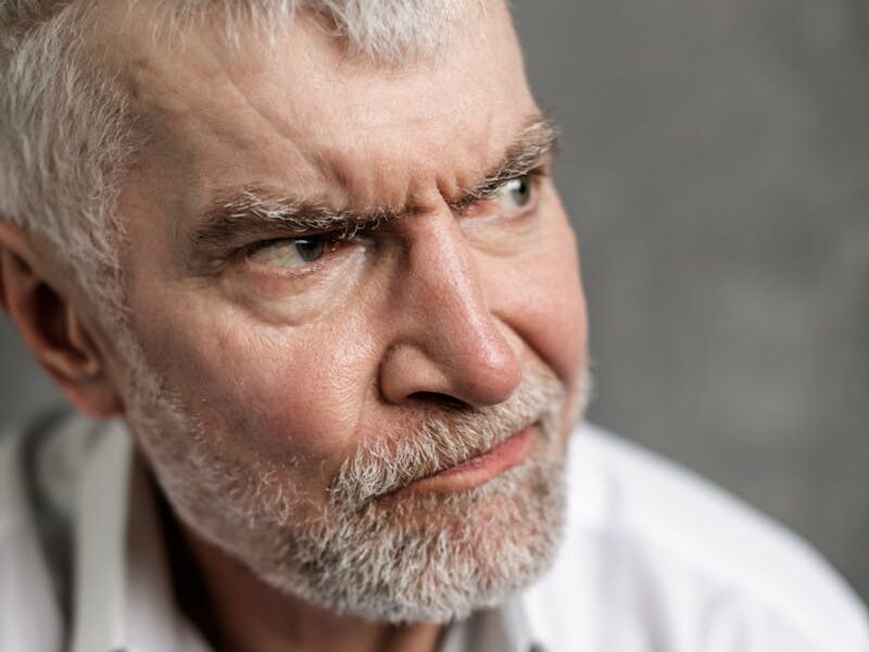 Portrait of a senior man with grey hair, looking pensive and serious, dressed in white shirt.