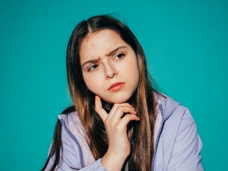 A young girl pondering deeply against a vibrant teal background.