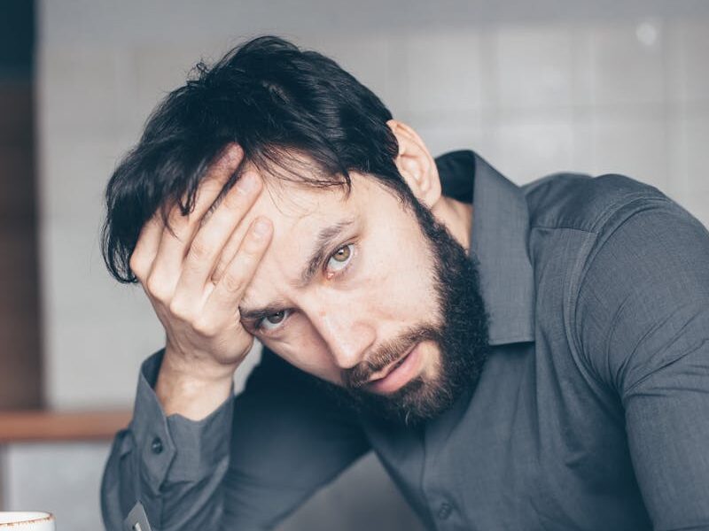 Thoughtful man sitting at a table with glasses and cup, showing frustration.