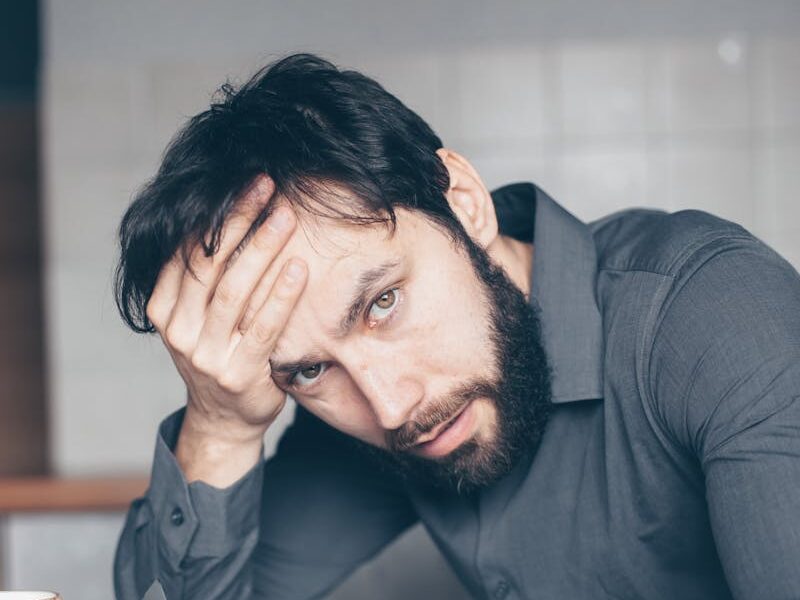 Thoughtful man sitting at a table with glasses and cup, showing frustration.