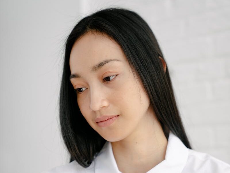 Peaceful ethnic female with long dark hair wearing white shirt sitting with cup of hot beverage and looking down