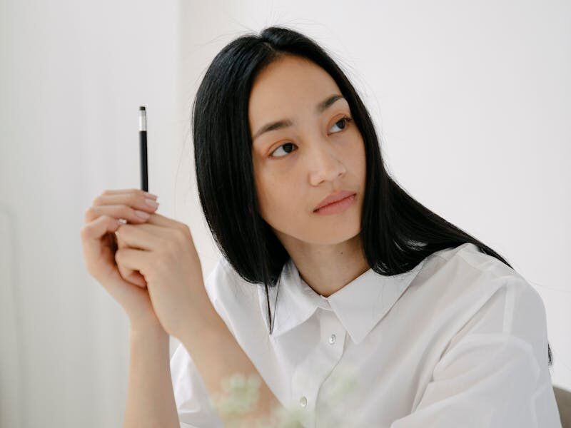 Thoughtful young woman looking away while studying at a desk in a minimalist setting.