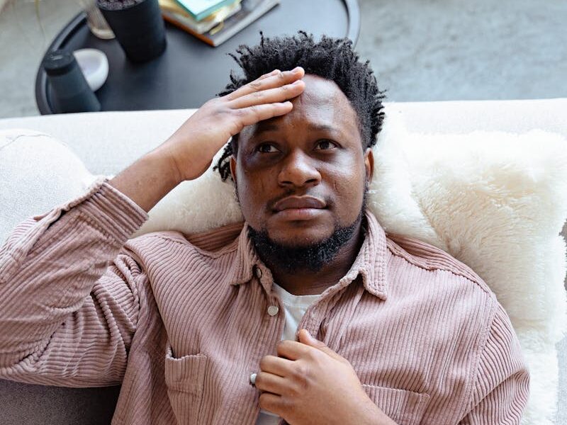 A man appears thoughtful while relaxing on a cozy sofa indoors.