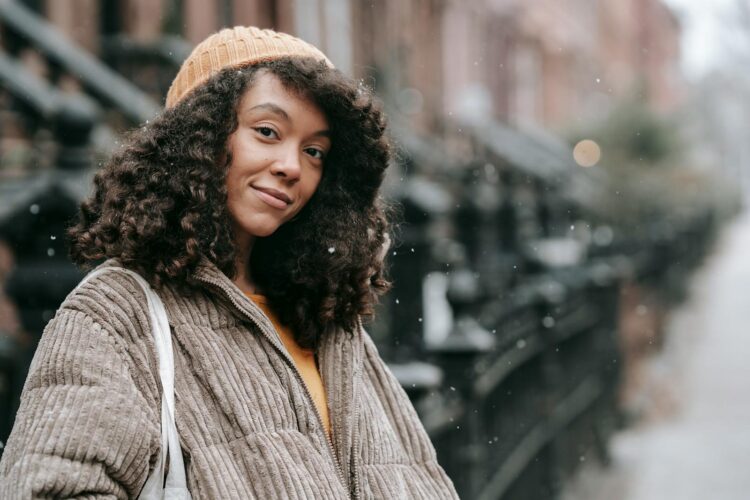 Young woman with curly hair smiles warmly on a snowy urban street.