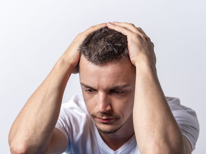 A man in distress sits with his head in hands on a blue chair indoors.
