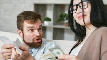 Interracial couple arguing over bills and cash at home.