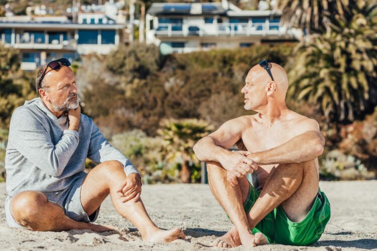Two older men enjoy a thoughtful conversation while sitting on a sunny beach.