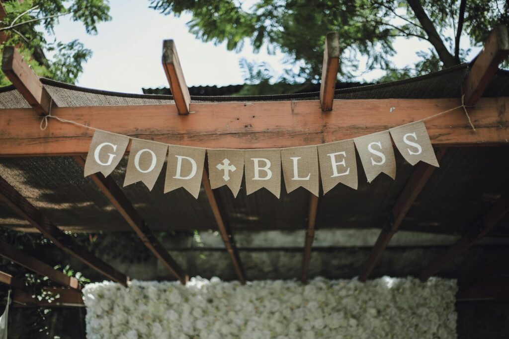 A charming pergola adorned with a 'God Bless' banner, set in a lush, outdoor environment.
