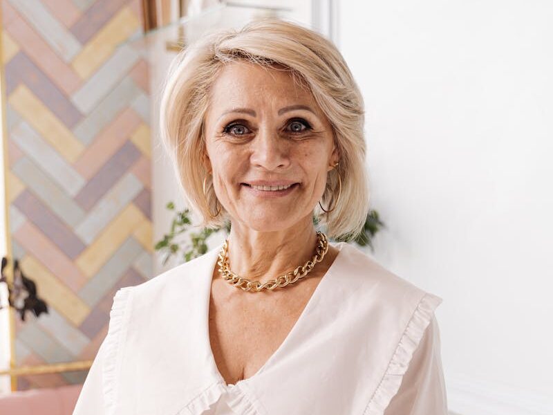 Smiling senior woman taking notes in a cozy, stylish room with pastel decor.