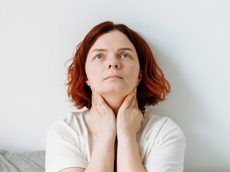 Contemplative woman with red hair touching her neck, exuding introspection in a calm environment.