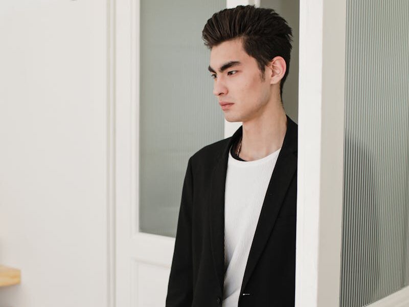 Asian man in formal attire standing at an open door, looking serious.