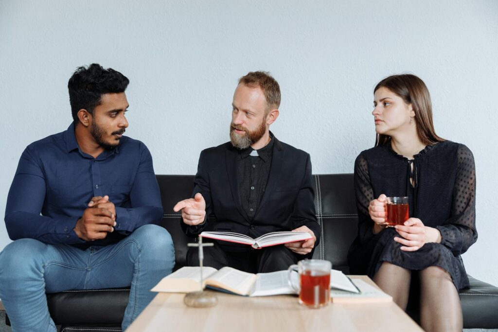 Diverse group of adults engaged in a religious discussion over tea indoors.