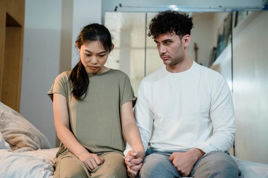 A couple sitting on a bed holding hands, facing relationship challenges indoors.