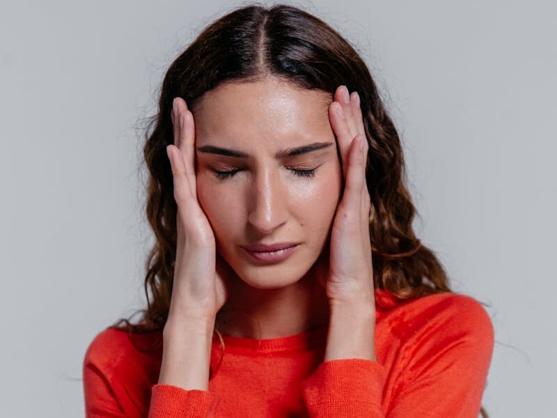A young woman in a red sweater holding her head, depicting stress or headache.