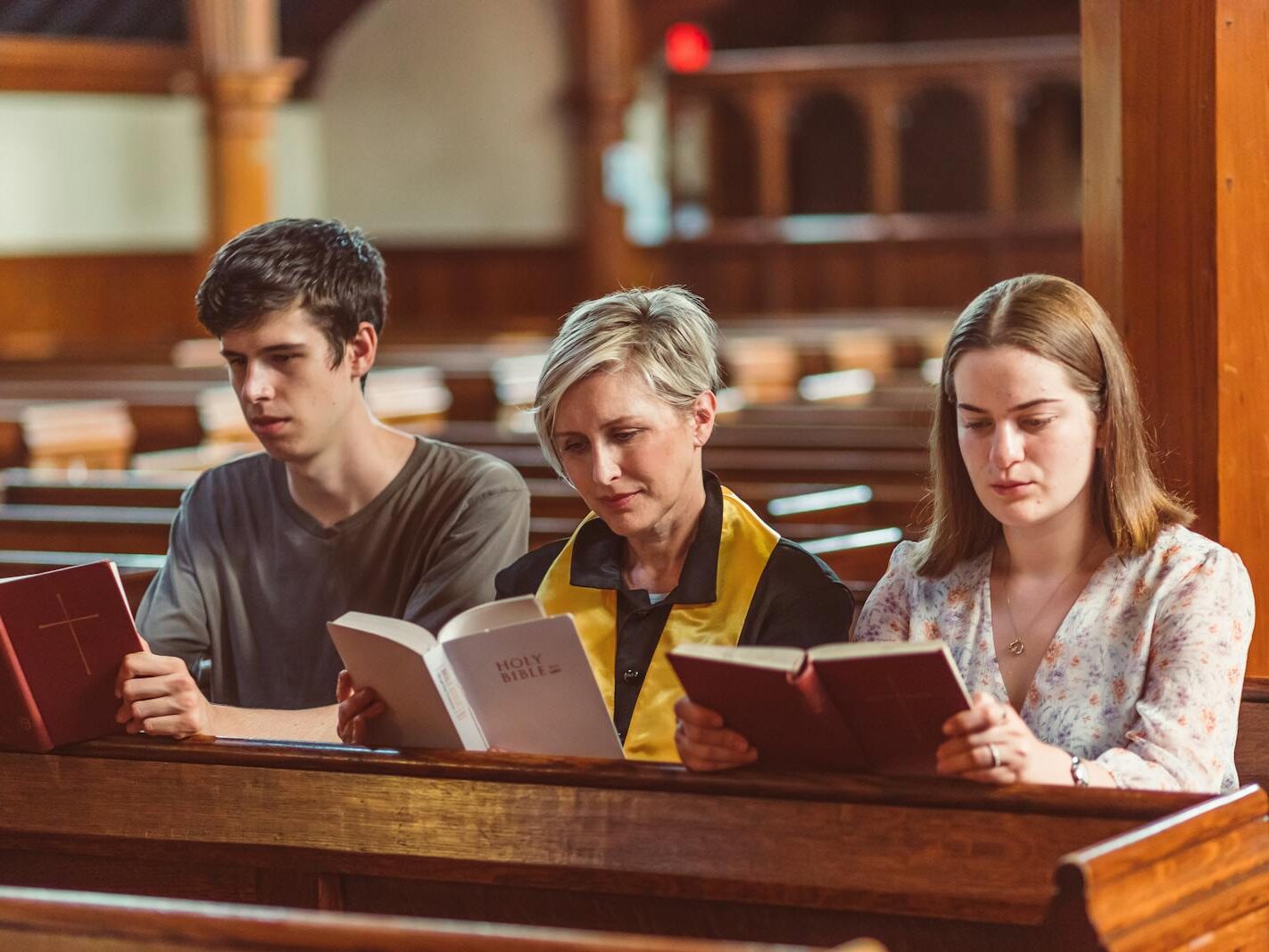 Three individuals reading bibles together in a church setting.