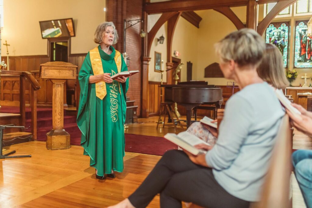 Elderly female clergy delivering a sermon to parishioners in a church setting.