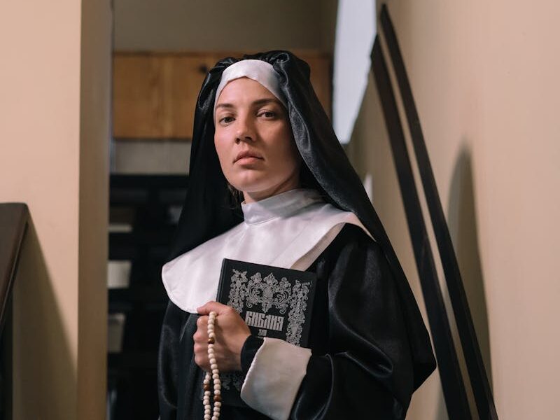 Portrait of a nun holding a rosary and Bible on a staircase, symbolizing faith and devotion.