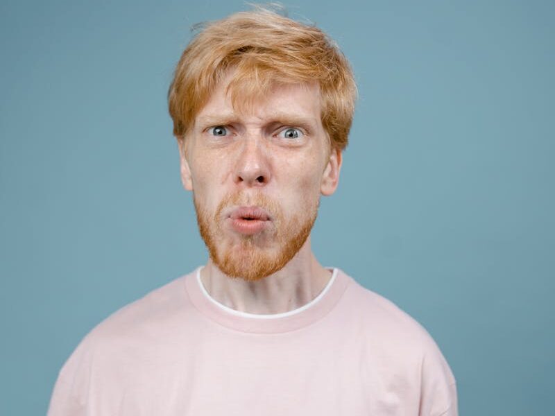 Adult man with angry facial expression in pink shirt, studio shot with blue background.