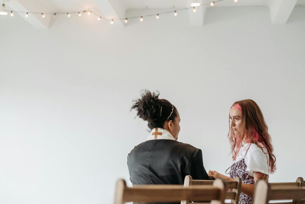 A woman pastor in a robe converses with another woman in a serene setting.