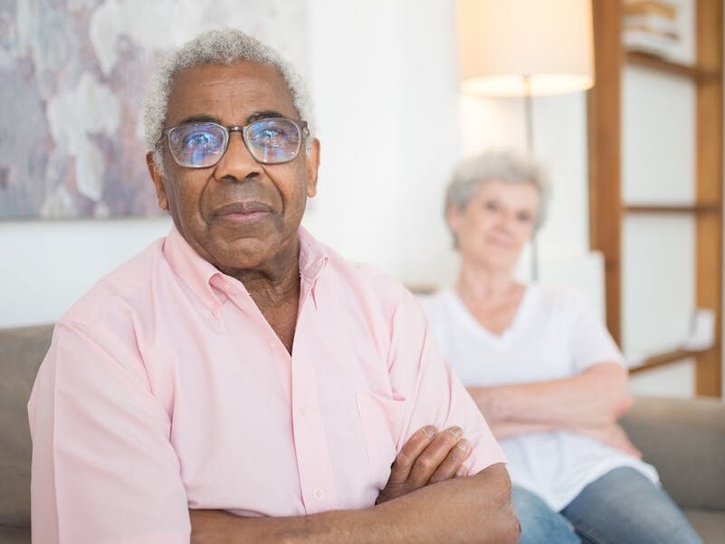 Senior adults relaxing with arms crossed on a couch in a cozy home setting.