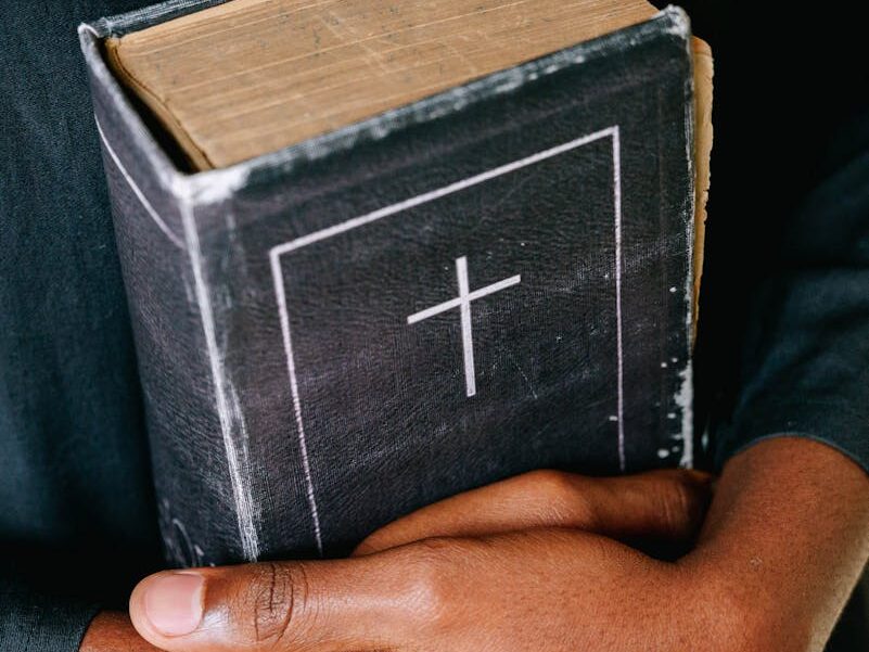 Close-up of hands holding a worn Bible featuring a cross symbol, symbolizing faith and spirituality.