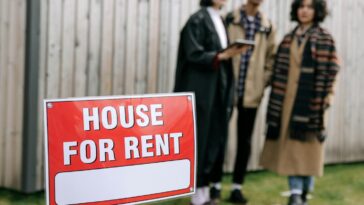 Three adults examining a house for rent sign outdoors, depicting diverse and inclusive interest in rental properties.