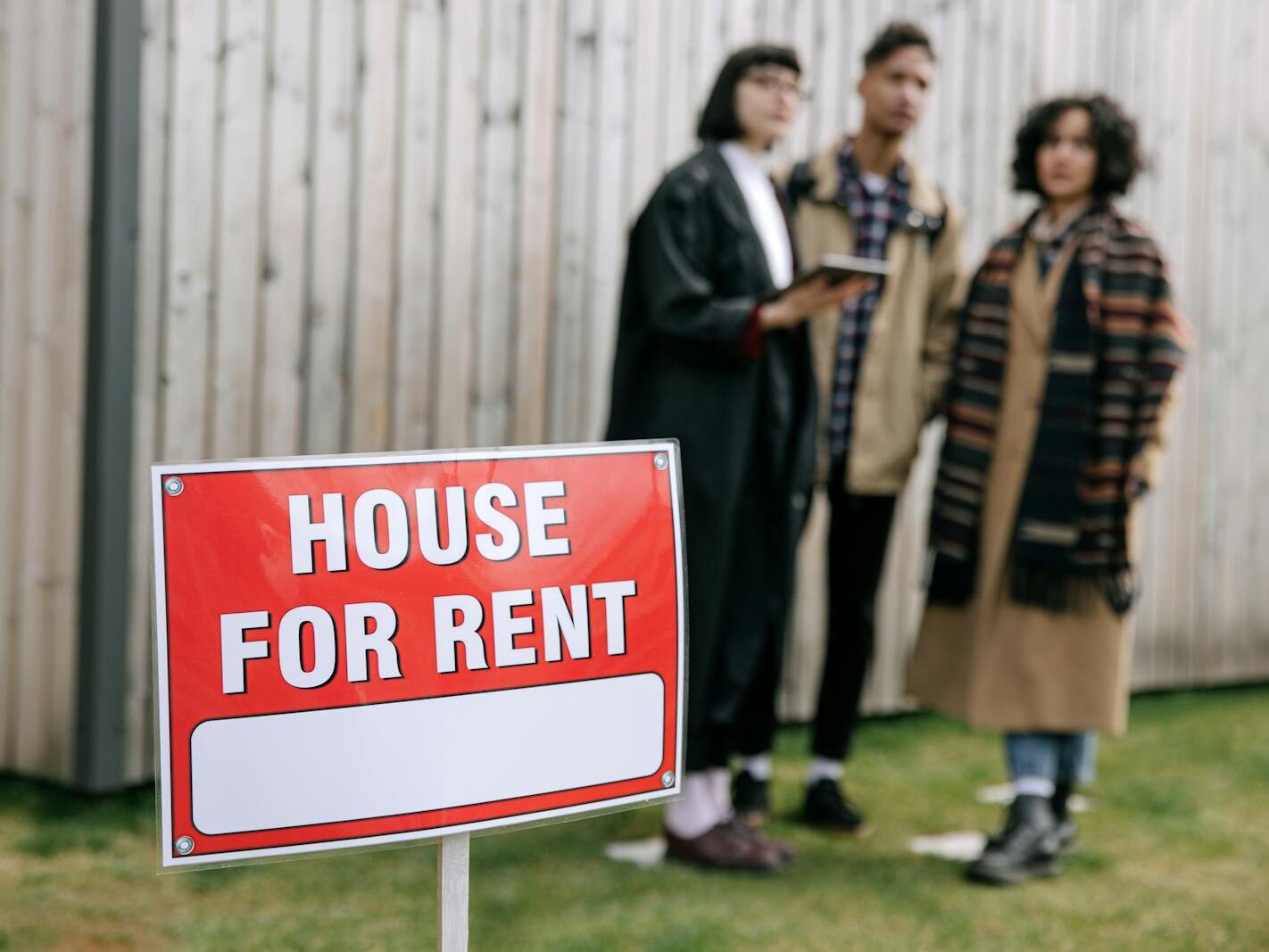 Three adults examining a house for rent sign outdoors, depicting diverse and inclusive interest in rental properties.