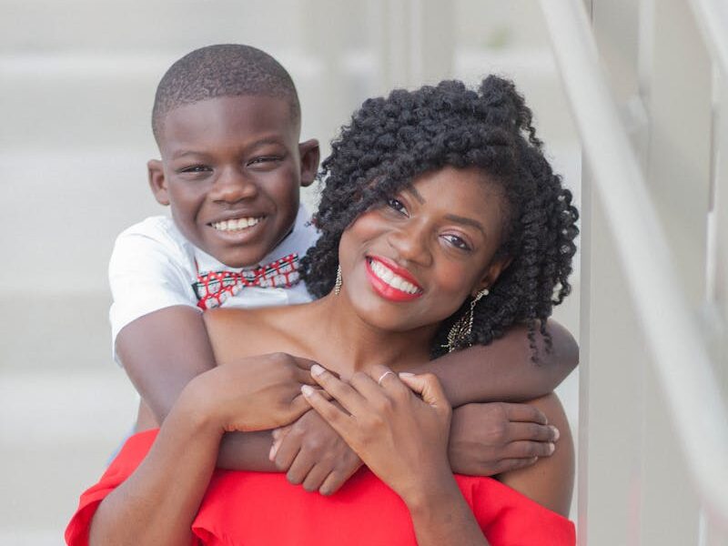 A cheerful African American mother and son share a loving hug on a staircase, both smiling brightly.