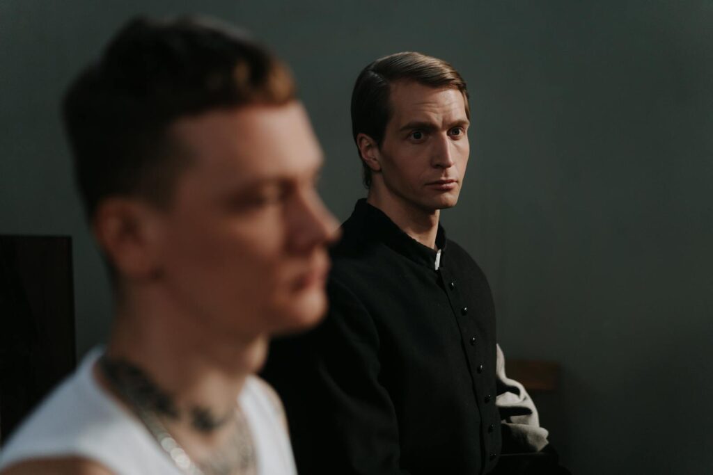 Two men, one in focus, sit thoughtfully indoors, highlighting contemplation.