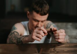 Tattooed man praying with a wooden crucifix inside a dimly lit church, symbolizing faith and reflection.