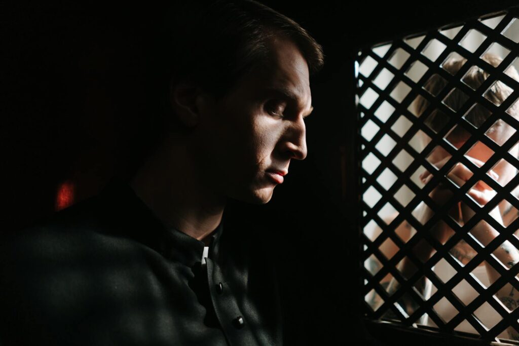A contemplative priest listens to a confession in a dimly lit church setting, capturing a moment of faith and spirituality.