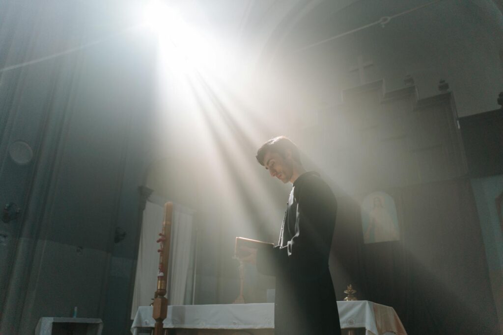A priest in a church is captured reading under a divine sunbeam, creating a serene religious atmosphere.