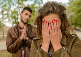A young man apologizes while a woman covers her face, set in an outdoor park.