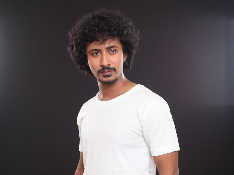 Portrait of a fashionable man in casual attire against a dark background, showcasing modern style.